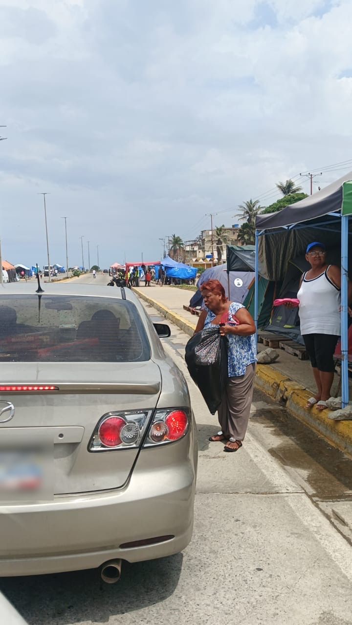 Calle con toldos y personas caminando junto a un carro estacionado. La placa del carro está difuminada.